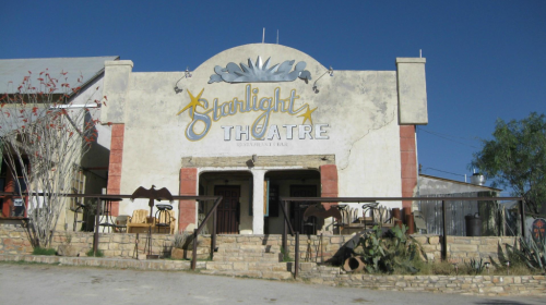 Exterior of Starlight Theatre with a faded sign, surrounded by a clear blue sky and sparse landscaping.