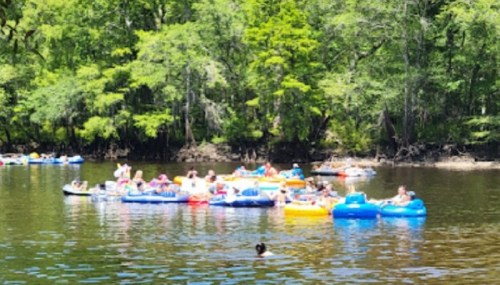 A group of people floating on colorful inner tubes in a river surrounded by lush green trees.