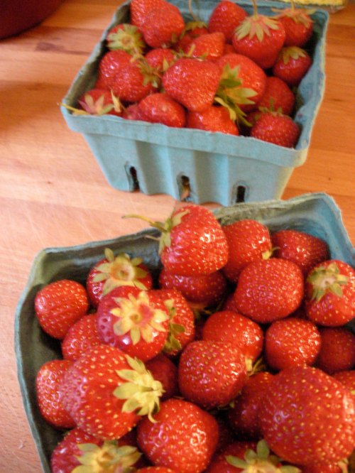 Two green baskets filled with fresh, ripe strawberries on a wooden surface.