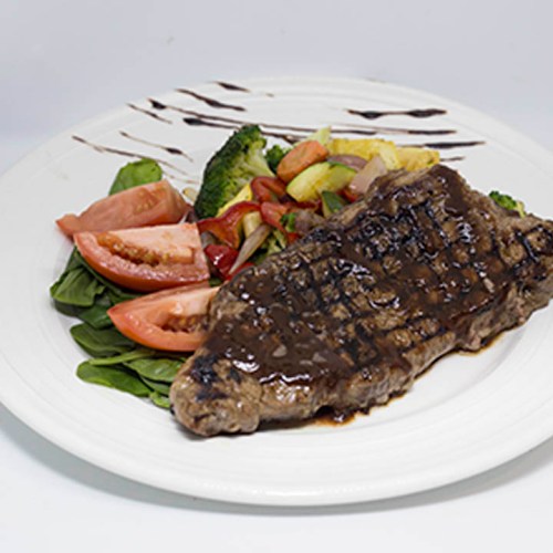 A grilled steak served with fresh vegetables, including broccoli, tomatoes, and spinach, on a white plate.