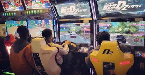 Three people playing racing arcade games in a colorful gaming arcade. Bright screens display vibrant racing scenes.