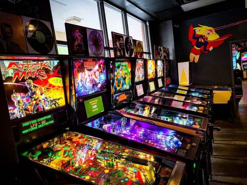 A row of colorful pinball machines in a game arcade, with vibrant artwork and illuminated playfields.