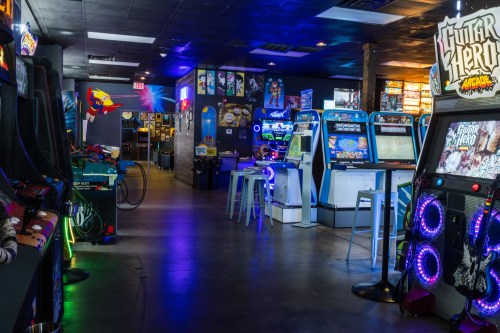 A vibrant arcade filled with colorful game machines and neon lights, featuring various classic and modern games.