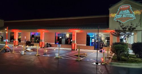 A brightly lit building at night with red lights, featuring a "STOP" sign projection and outdoor seating.