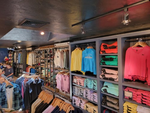 A clothing store interior featuring colorful shirts and hoodies neatly arranged on shelves and hangers.