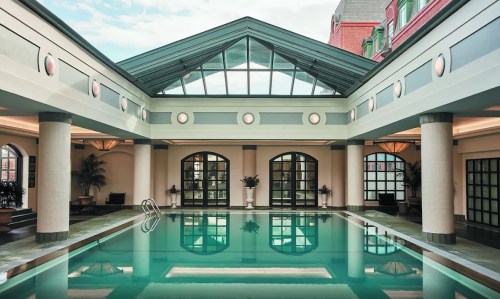 Indoor swimming pool with large windows, modern architecture, and lush greenery surrounding the area.