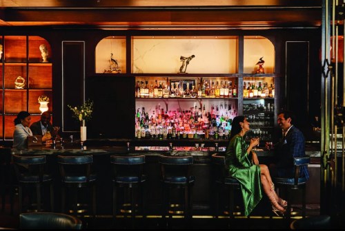 A stylish bar scene with two couples enjoying drinks, surrounded by shelves of colorful liquor bottles.