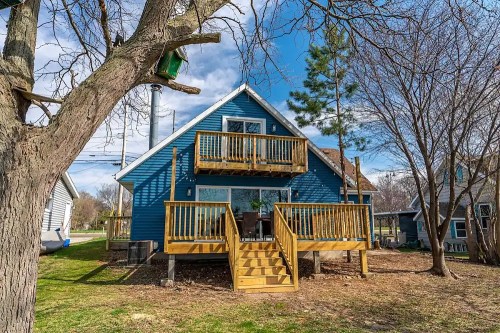 A blue house with wooden decks surrounded by trees and a grassy yard on a sunny day.