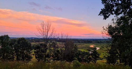 A serene landscape at sunset, featuring a river winding through lush greenery under a colorful sky.