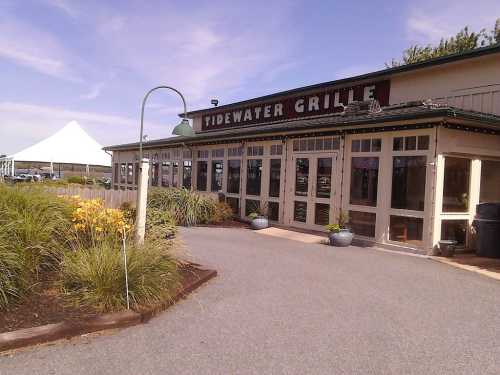 Exterior of Tidewater Grille, featuring large windows, a tent in the background, and landscaped greenery.