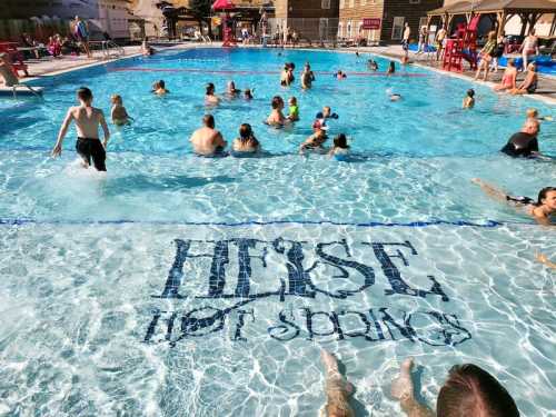 A busy pool scene with people swimming and relaxing, featuring the words "Heise Hot Springs" on the pool floor.