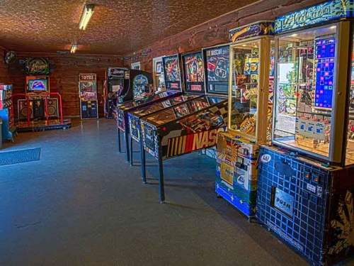 A retro arcade room filled with various pinball machines and arcade games, featuring a NASCAR-themed pinball table.