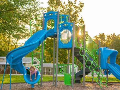 A colorful playground with slides and climbing structures, featuring a child sliding down as the sun sets in the background.