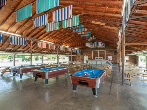 Interior of a spacious hall with pool tables and picnic-style seating, decorated with colorful flags.