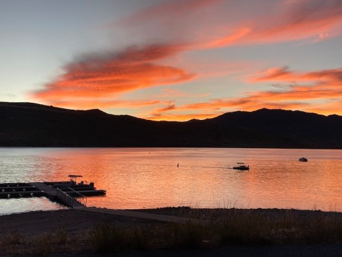 A serene sunset over a lake, with vibrant orange clouds reflecting on the water and boats in the distance.