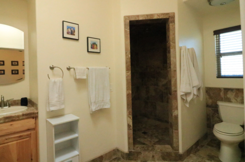 A clean bathroom featuring a shower, toilet, sink, and decorative wall art. White towels hang neatly on racks.