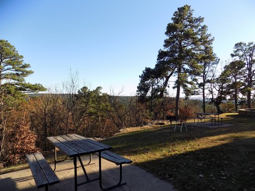 A scenic view of a park with picnic tables, trees, and a clear blue sky in the background.