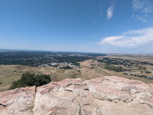 A panoramic view from a rocky outcrop overlooking a valley and distant hills under a clear blue sky.