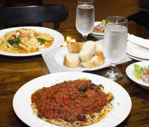 A table set with plates of pasta, a bowl of bread, and glasses of water, featuring a dish of spaghetti with marinara sauce.