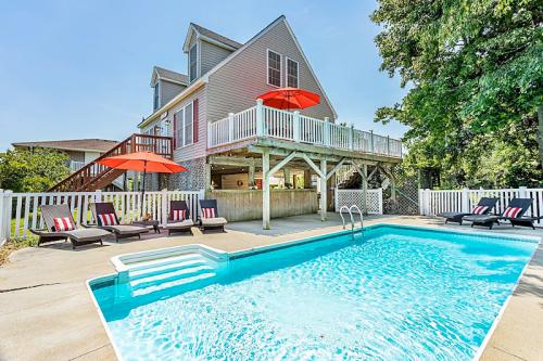 A backyard with a swimming pool, lounge chairs, and a house with a deck and red umbrellas.