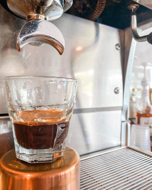 A glass sits under an espresso machine, capturing a fresh shot of dark coffee.