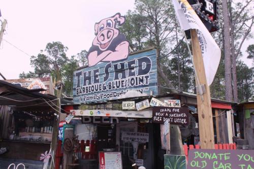 A rustic barbecue restaurant sign featuring a cartoon pig, surrounded by trees and colorful decorations.