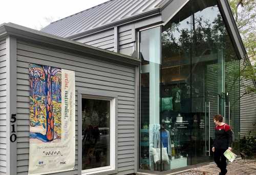 A modern building with a glass facade and a colorful art poster, featuring a person walking by.