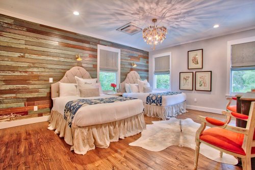 Cozy bedroom with two beds, rustic wood walls, a chandelier, and stylish decor, creating a warm, inviting atmosphere.