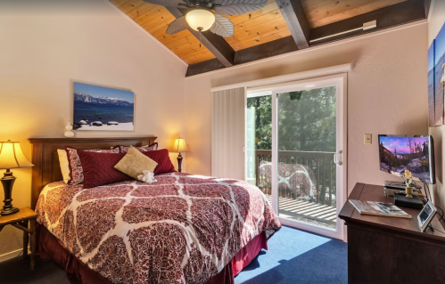 Cozy bedroom with a queen bed, wooden ceiling, and sliding door leading to a balcony with scenic views.