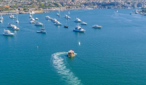 Aerial view of a marina with numerous boats and a small floating structure creating ripples in the water.