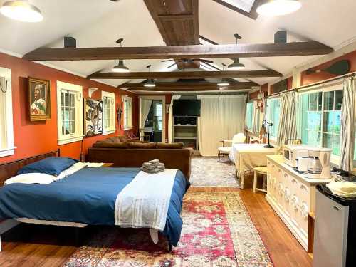 Cozy interior of a spacious room with a bed, sofa, and rustic decor, featuring large windows and wooden beams.