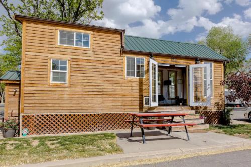 A small wooden house with a green metal roof, featuring open double doors and a picnic table in front.