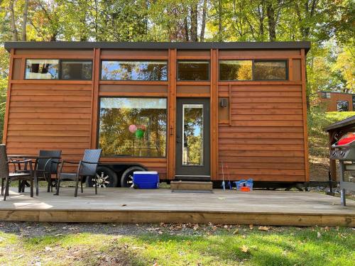 A modern tiny house with wooden siding, large windows, and a deck surrounded by trees in a serene outdoor setting.