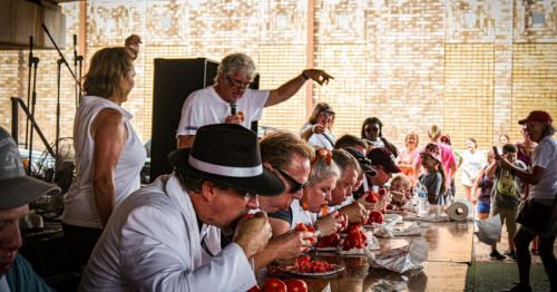 A group of contestants compete in a tomato-eating contest while an announcer gestures in the background.