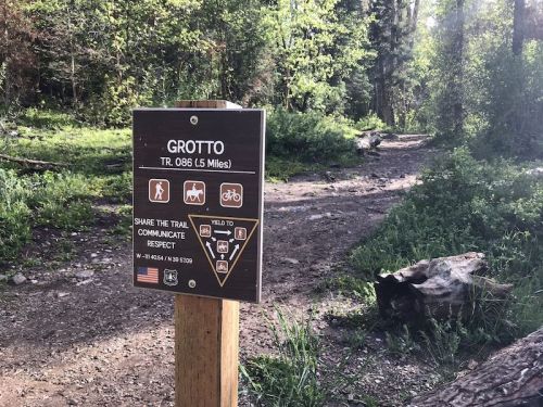 Trail sign for Grotto (TR 086, 5.5 miles) in a forested area, with guidelines for sharing the trail.