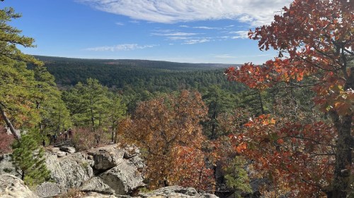 A scenic view of a forested landscape with autumn foliage and rocky outcrops under a blue sky with clouds.