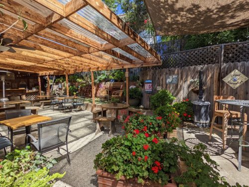 A cozy outdoor patio with wooden beams, tables, and vibrant flowers, creating a welcoming atmosphere.
