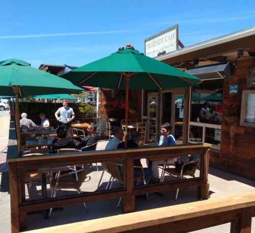 Outdoor seating area of Trailside Cafe with green umbrellas, people dining, and a sunny blue sky.