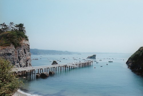 A serene coastal scene featuring a wooden pier extending into calm waters, surrounded by boats and rocky cliffs.