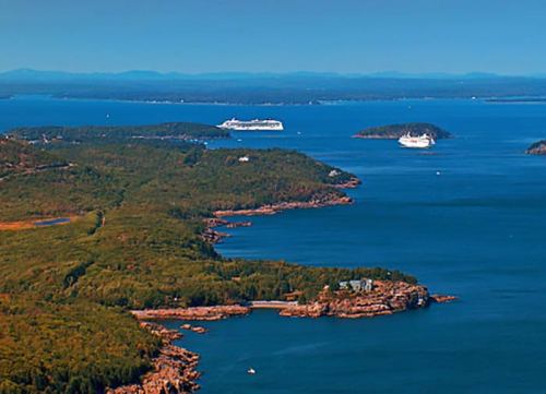 Aerial view of a coastal landscape with islands, ships, and lush greenery under a clear blue sky.