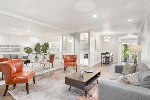 Modern living room with orange chairs, a gray sofa, a coffee table, and a mirrored wall, featuring stylish decor.