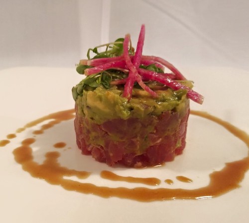 A beautifully plated dish featuring tuna tartare layered with avocado, garnished with pickled radish and microgreens.