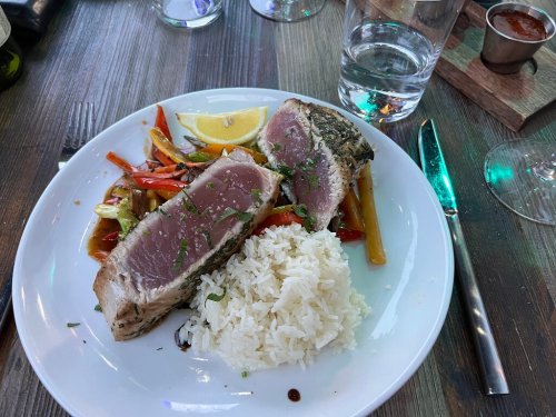 A plate of seared tuna steak with colorful sautéed vegetables and a side of white rice, garnished with lemon.