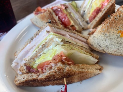 A close-up of a sandwich with layers of turkey, lettuce, tomato, and bacon on whole grain bread, served on a plate.