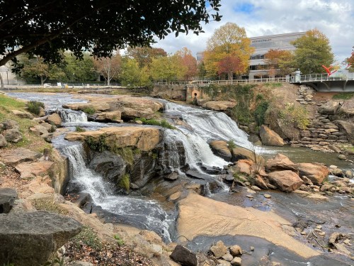 A scenic view of a waterfall cascading over rocks, surrounded by trees and a building in the background.
