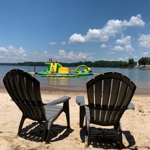 Two gray chairs on a sandy beach, overlooking a colorful inflatable water park and a clear blue sky.