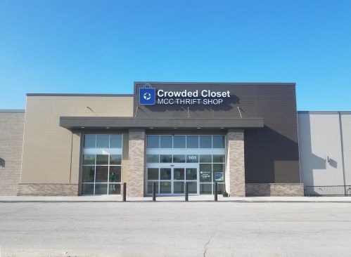 Exterior of Crowded Closet MCC Thrift Shop, featuring a large sign and glass entrance under a clear blue sky.