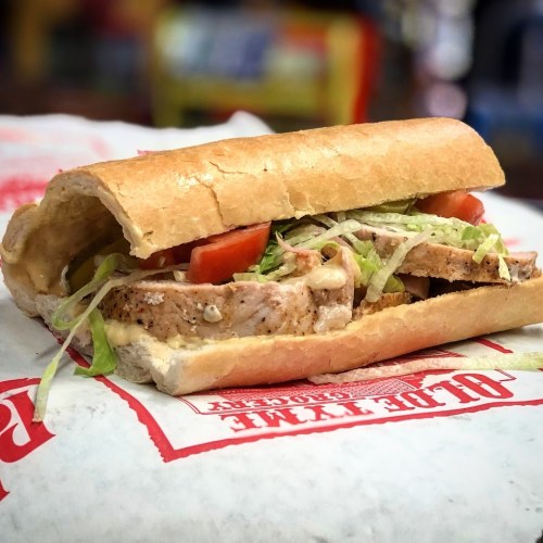 A close-up of a sandwich with grilled chicken, lettuce, tomato, and sauce, served in a toasted sub roll.
