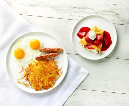 A plate with two sunny-side-up eggs, sausage links, and hash browns, alongside a dessert of crepes with strawberries and whipped cream.