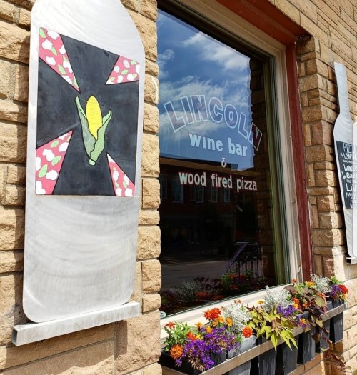 A window of Lincoln Wine Bar featuring colorful artwork and flowers in the foreground.
